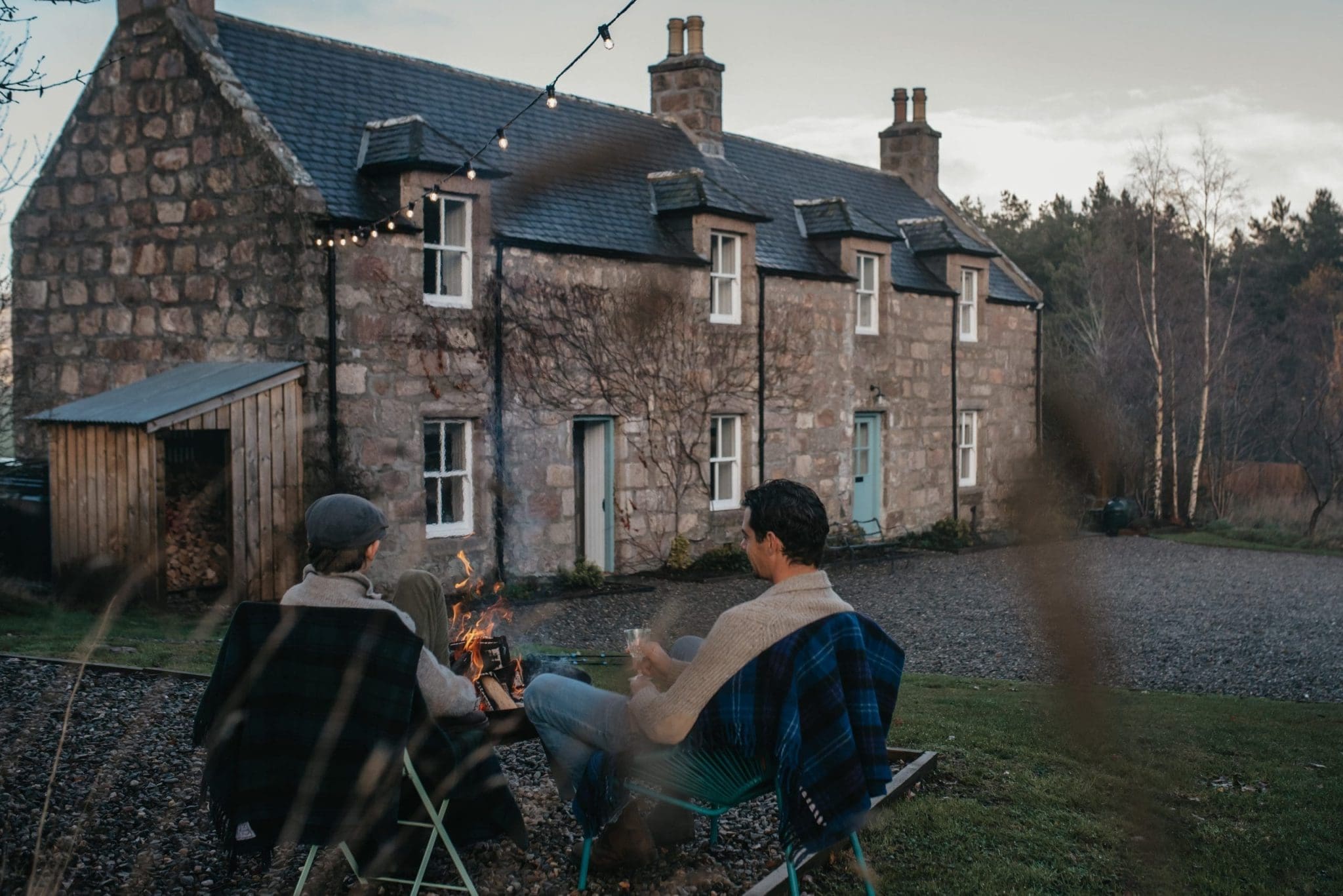 Guests enjoying a late afternoon in autumn, sat close to an outdoor wood burning fire.