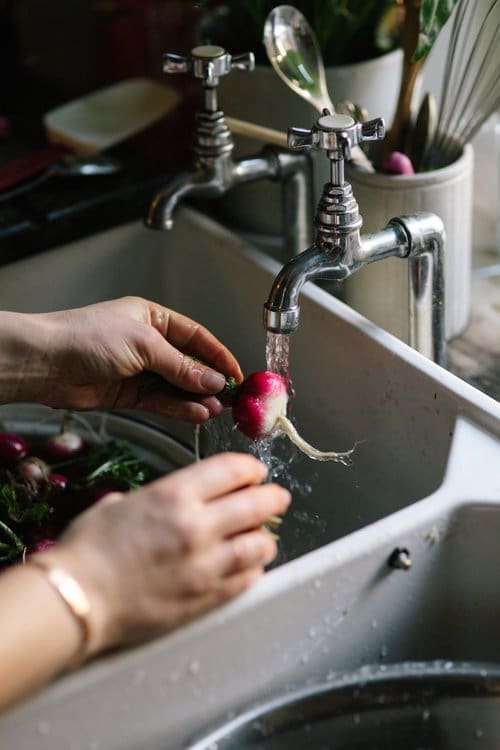 A single horseradish being washed under a tap in the kitchen sink