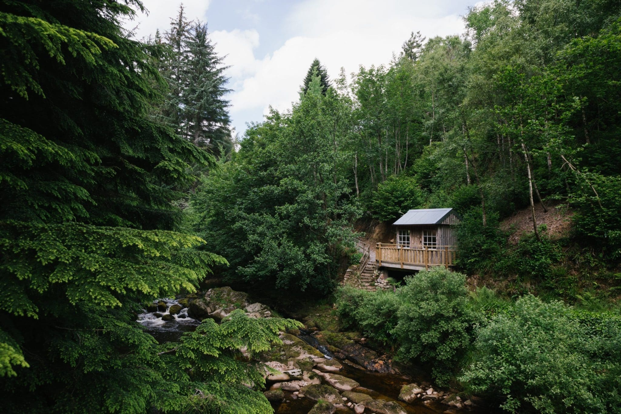 An image from the North Lodge Cabin collection. A cabin in the distance overlooking a river and surrounded by trees.