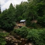 An image from the North Lodge Cabin collection. A cabin in the distance overlooking a river and surrounded by trees.