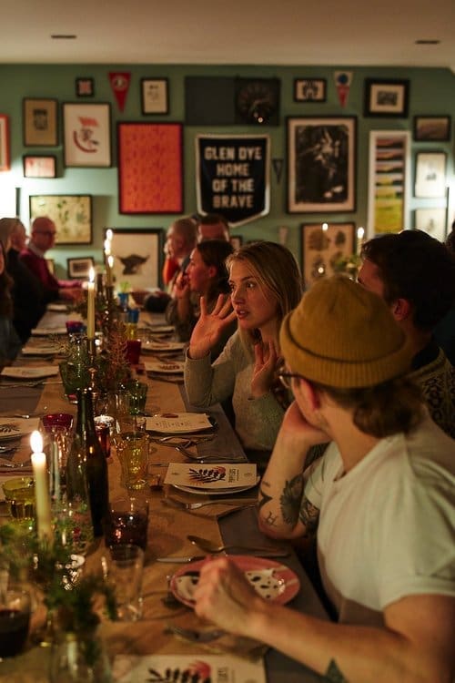Guests seated at a long dining table enjoying good company and ready to be served some delicious food