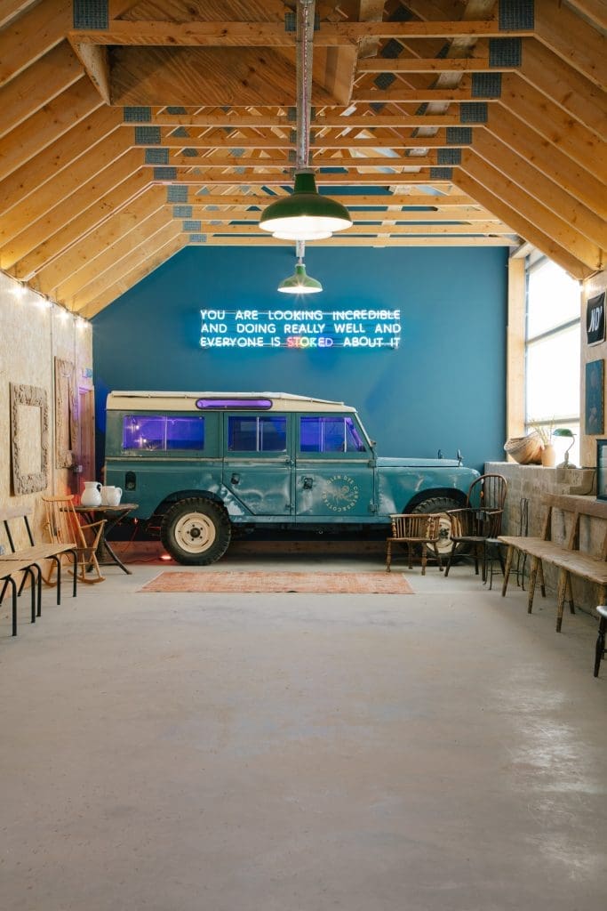 A custom neon sign placed on the wall of Glen Dyes cinema that reads "You are looking incredible and doing really well and everyone is stoked about it" above an old Land Rover Discovery.